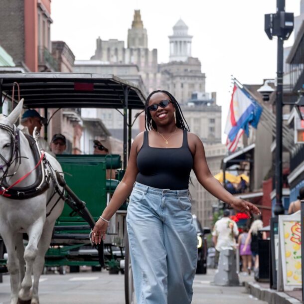 Simone Cheri walking down Bourbon Street with a horse-drawn carriage and people in the background